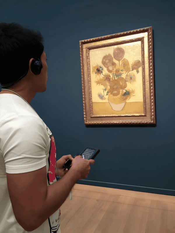 Visitor using an audio guide to view Vincent van Gogh’s Sunflowers in a museum gallery.