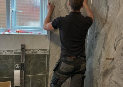 Person installing bathroom wall panels near window.