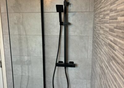 Modern shower with glass screen and tiled walls.