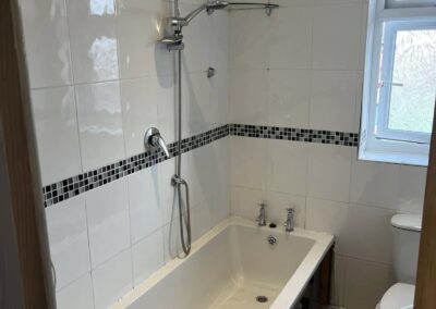 Small bathroom with white tiled bathtub and shower.