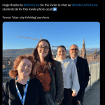 A group photo on the Ulster University rooftop, with people smiling at the camera with a lovley blue sky in the background.