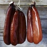 Smoked sausages hanging on strings against a wooden background.