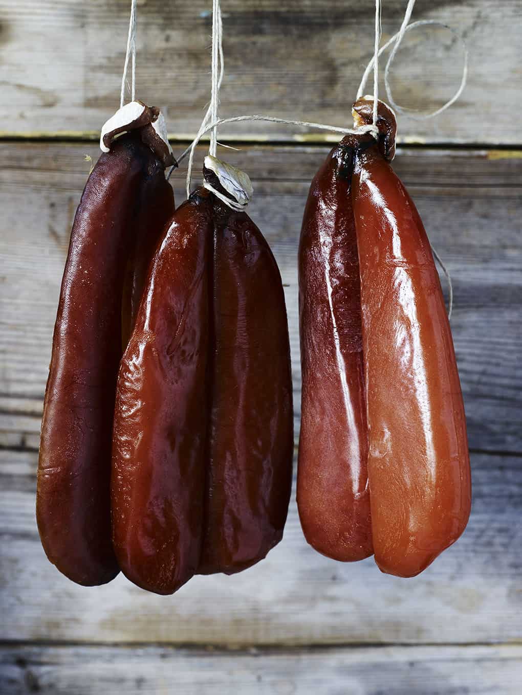 Smoked sausages hanging on strings against a wooden background.