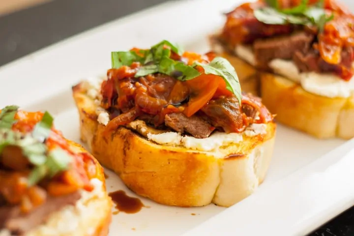 Steak bruschetta with goat cheese and tomato jam on toasted bread.