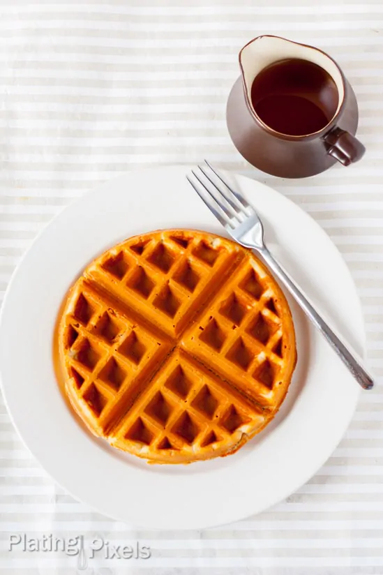 Delicious gluten-free waffles with maple syrup and peanut butter on a white plate.