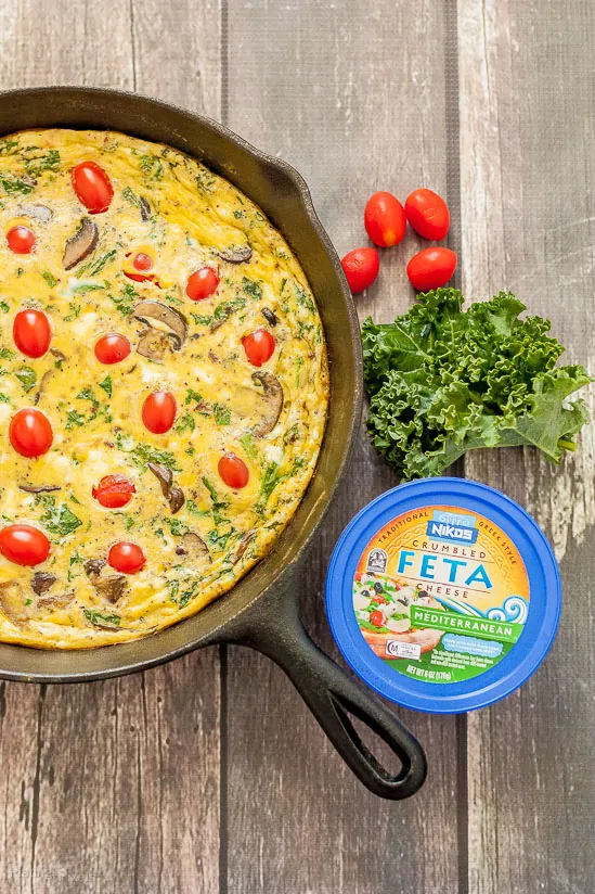 Kale and feta frittata with cherry tomatoes and fresh kale on a rustic wooden table.