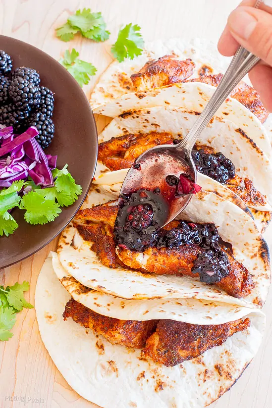 Fish tacos with blackberry balsamic salsa and fresh herbs on a white plate.