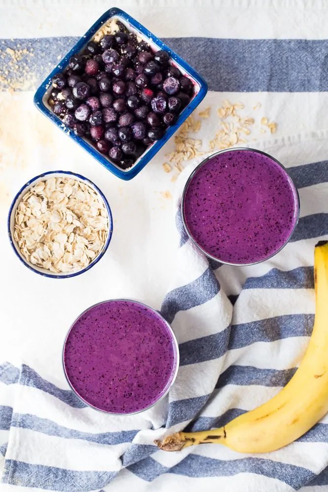 Blueberry peanut protein smoothie with fresh blueberries and banana on a striped cloth.