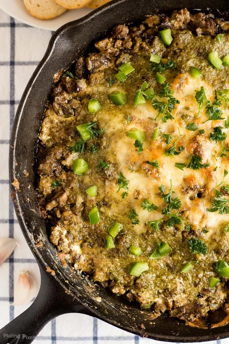 Sausage and pesto pizza dip in a skillet with melted cheese and green onions.