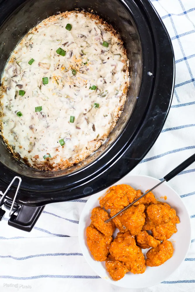 Creamy blue cheese sauce in slow cooker with green onions, served with crispy chicken bites.