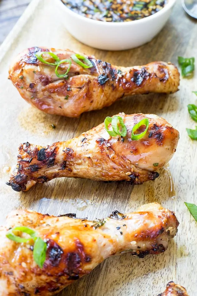 Juicy grilled chicken drumsticks with ginger sesame glaze and green onion garnish.