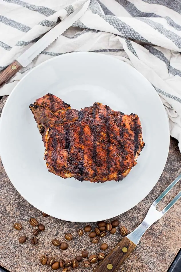 Juicy grilled pork chop seasoned with cowboy coffee rub on a white plate.