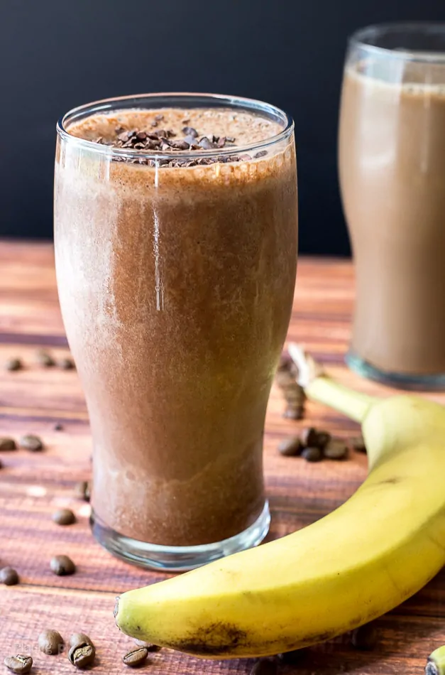 Chocolate banana mocha smoothie with coffee beans and banana on wooden table.