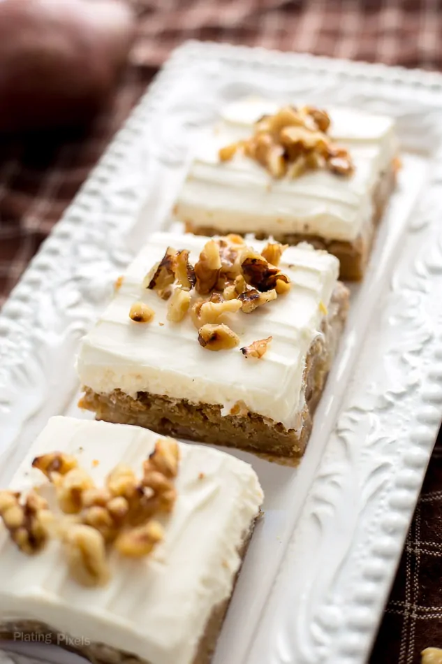 Frosted maple pear blondies topped with chopped nuts on a white platter.