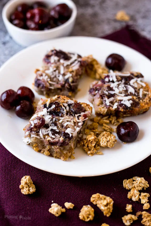 Cherry orange oatmeal bars with coconut flakes and fresh cherries on a white plate.