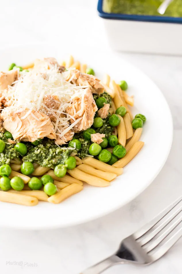 Salmon pesto pasta with green peas and grated cheese on a white plate.