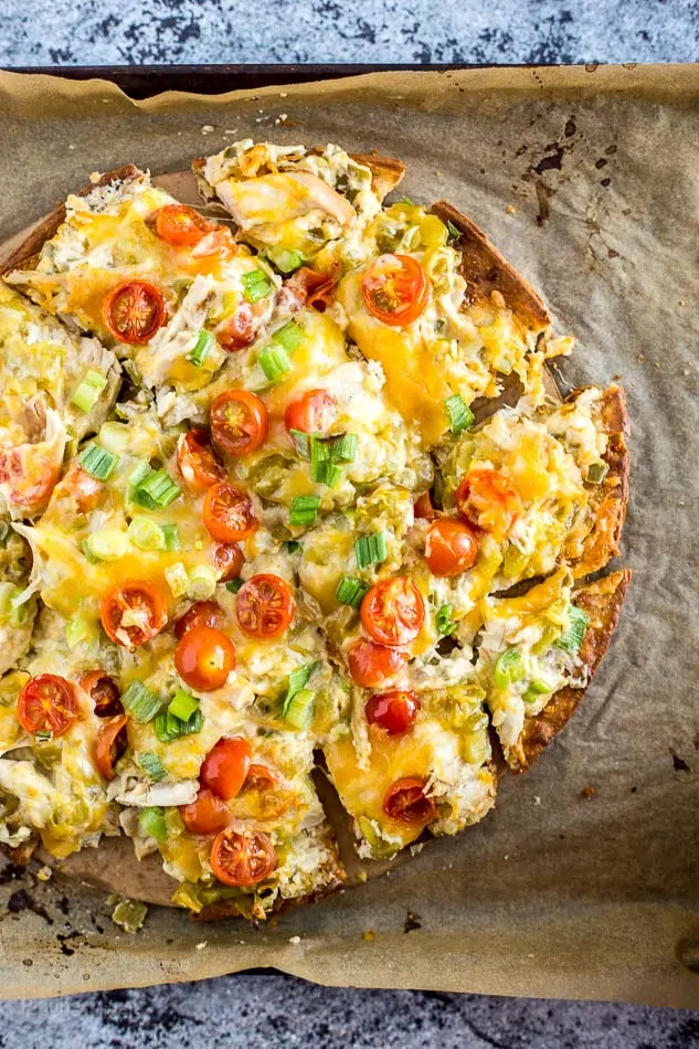Close-up of cheesy chicken and chile flatbread pizza with cherry tomatoes and green onions.