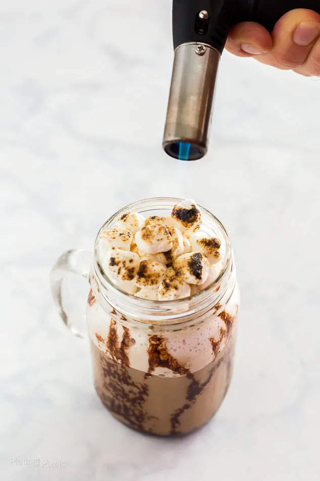 Toasted marshmallows on a s'mores frappe with a torch, perfect for a frozen cappuccino treat.