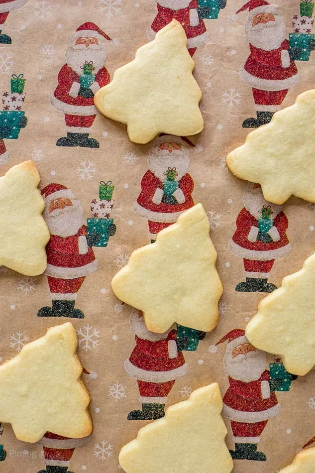 Christmas tree-shaped sugar cookies on holiday-themed parchment paper.