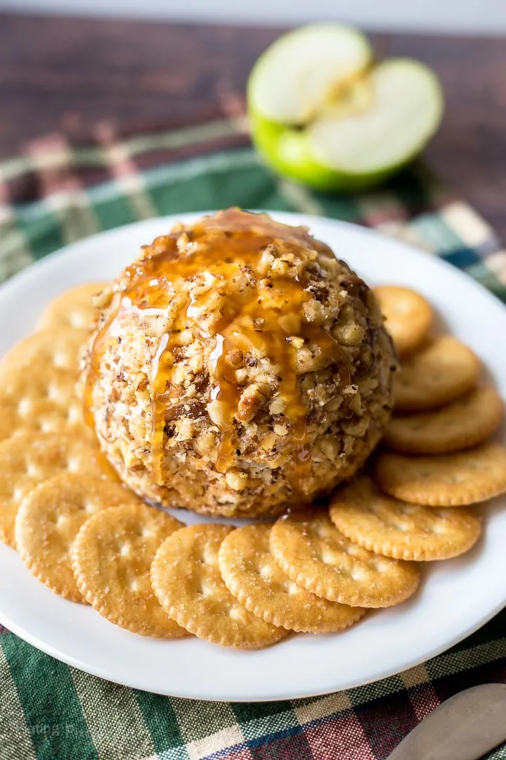 Caramel apple cookie ball with crushed nuts on a white plate with crackers and apple slices.