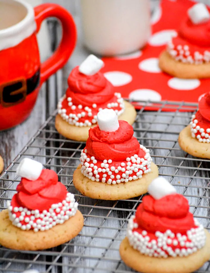 Decorated Christmas cookies with red frosting and white sprinkles on a cooling rack.