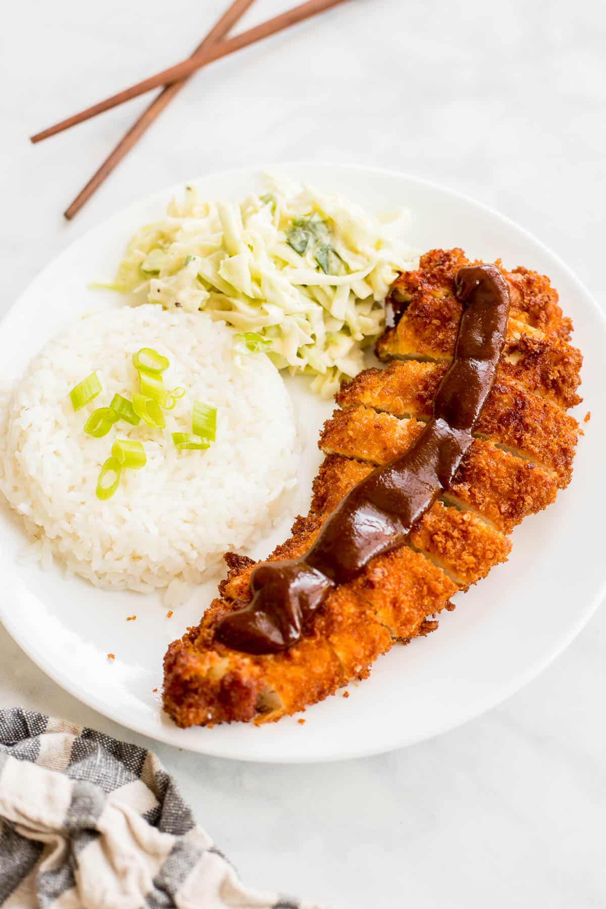 Crispy breaded chicken Katsu with Tonkatsu sauce served with white rice and creamy coleslaw on a white plate