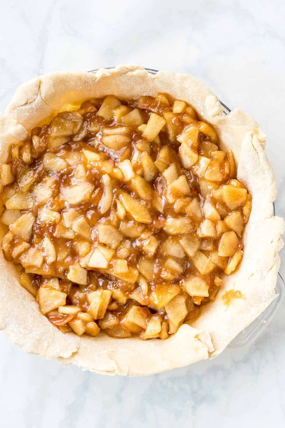 homemade apple pie filling over pie crust in a pie pan Apple pie filling with diced apples and caramelized sugar in a pie crust.