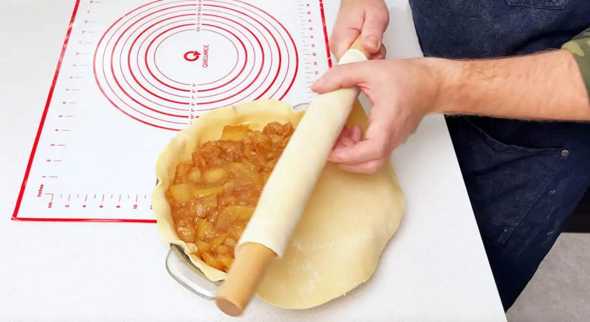placing top piece of pie dough over apple pie filling in. a pie pan placing top piece of pie dough over apple pie filling in a pie pan