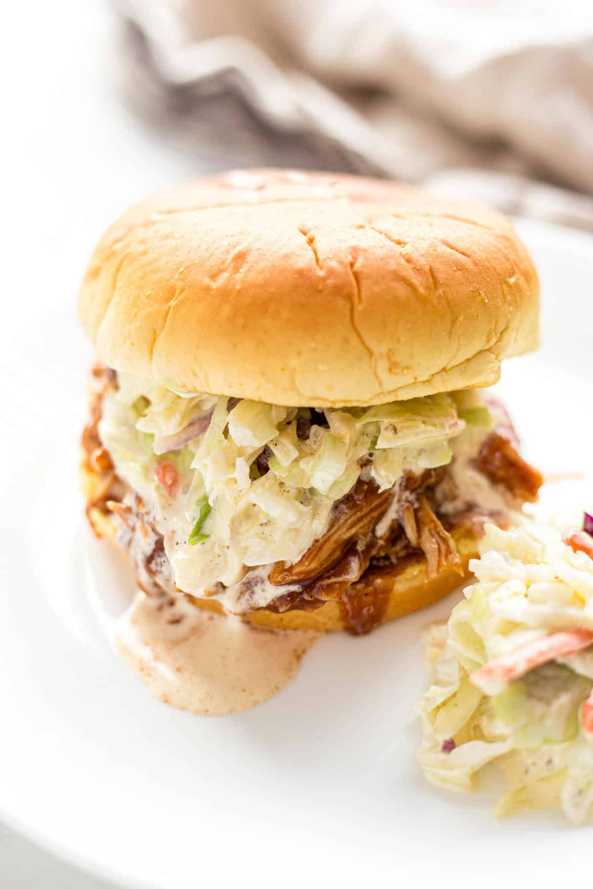 Pulled chicken sandwich with homemade coleslaw on a white plate.