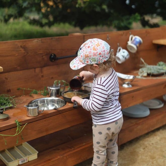 Child playing with pretend outdoor kitchen, children’s imaginative play, nature-based activity, woodland adventure, playful learning.
