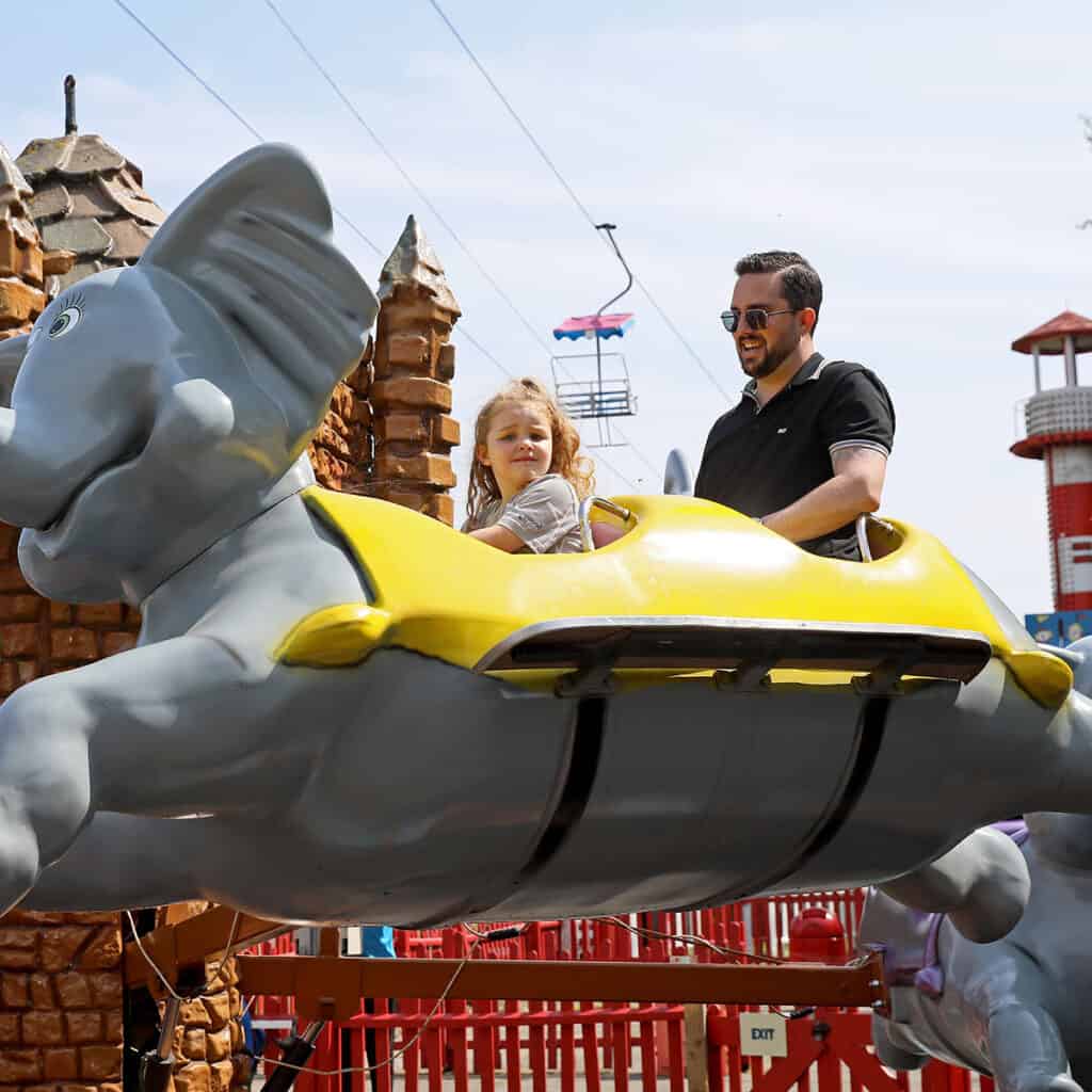 Man and young girl on elephant themed theme park ride