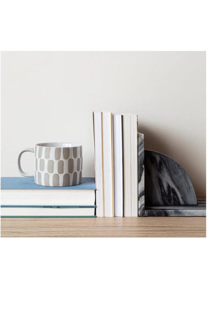 Bookshelf with a stack of journals, a ceramic mug, and a marble bookend, showcasing organization and planning for productivity.