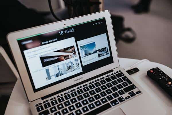 Open MacBook displaying a website with multiple images and text, placed on a desk with a remote control nearby.
