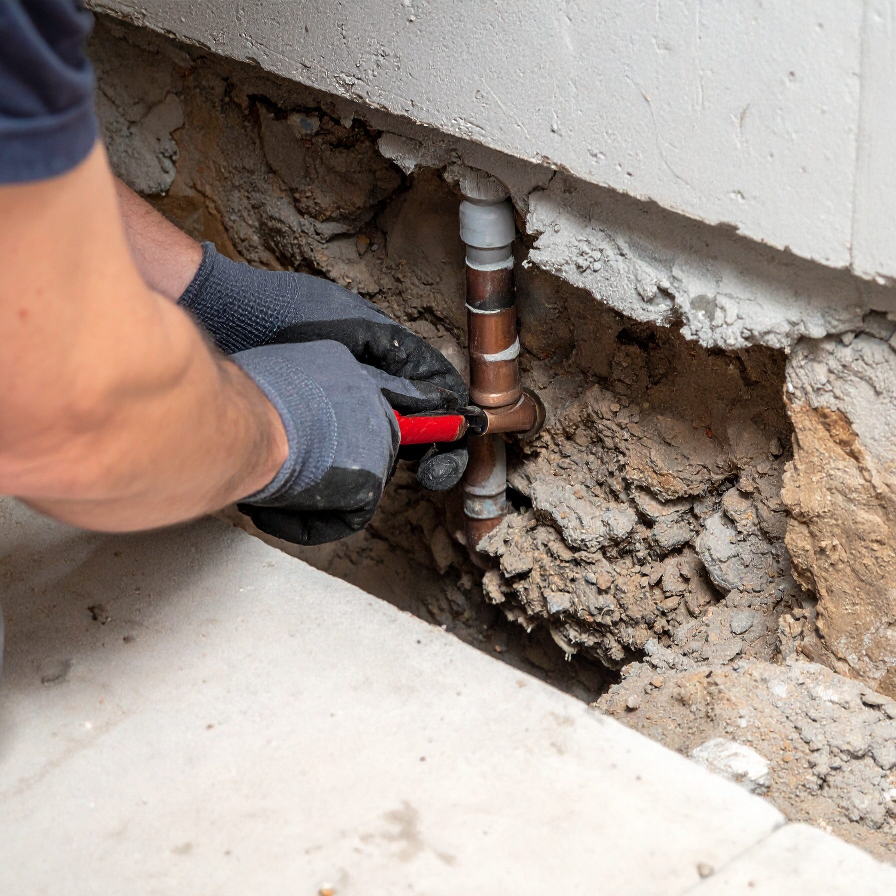 Firefly_Close-up of gloved hands repairing a leaking copper water pipe beneath a concrete sla 942430