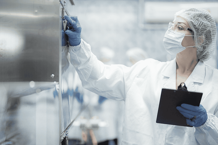 Lab technician inspecting equipment and documenting results during a cleanroom quality‑control check.