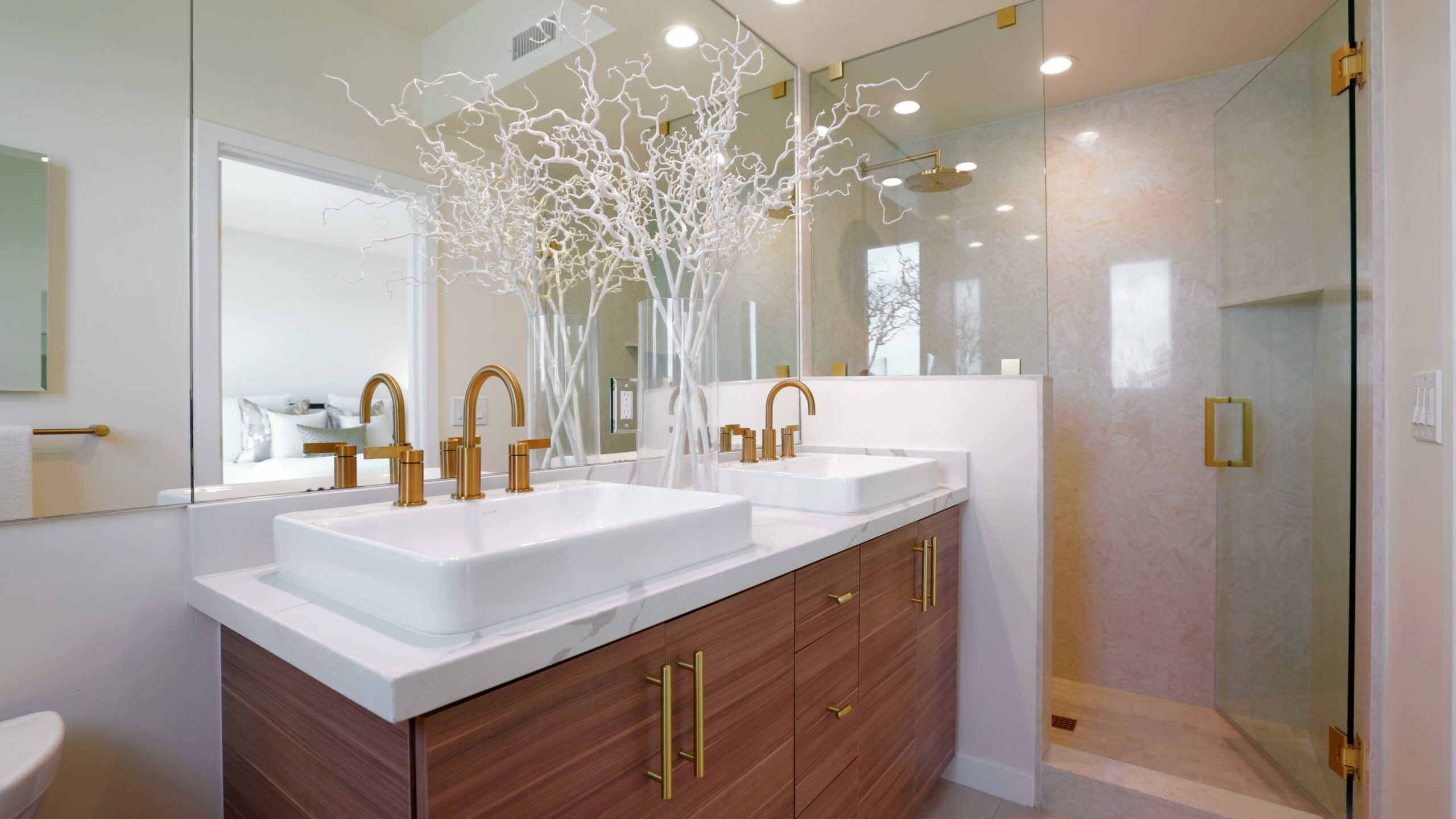 Luxurious bathroom with double white vessel sinks, gold fixtures, and a modern glass-enclosed shower, featuring elegant decor and contemporary design at Point North Park – San Diego, California.