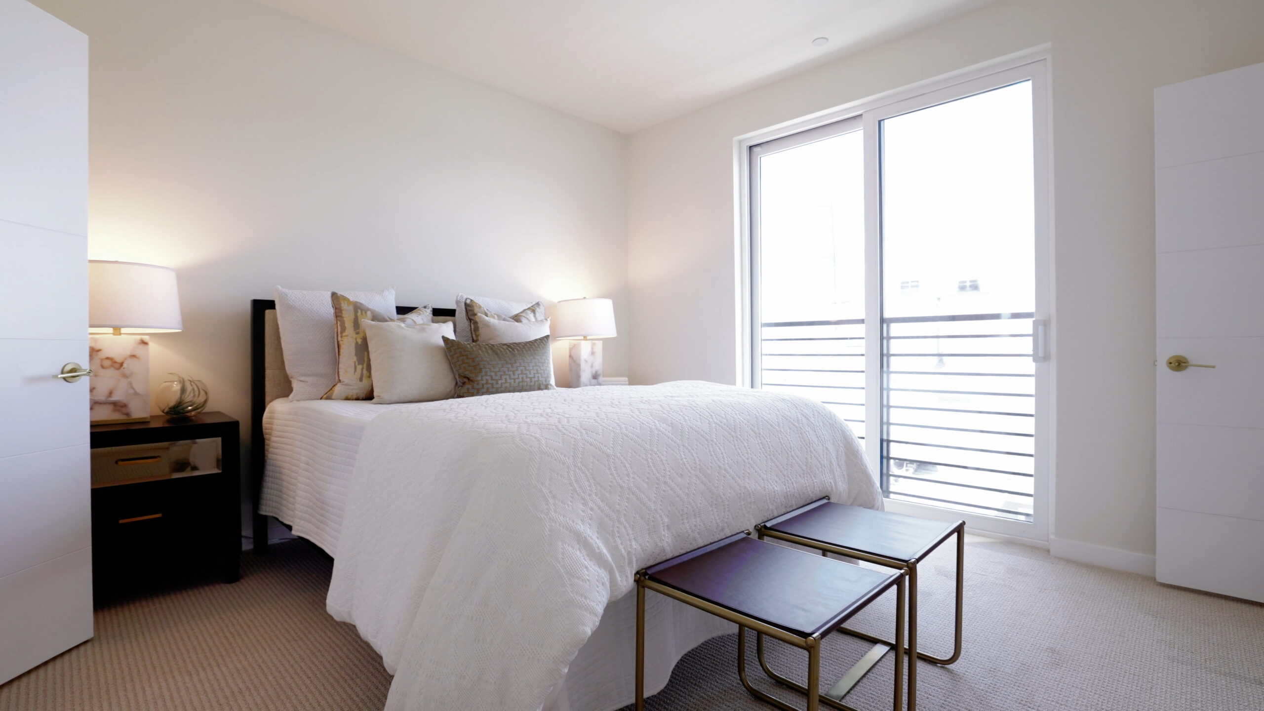 Modern bedroom with white bedding, decorative pillows, and natural light from large sliding glass doors at Point North Park in San Diego, California.