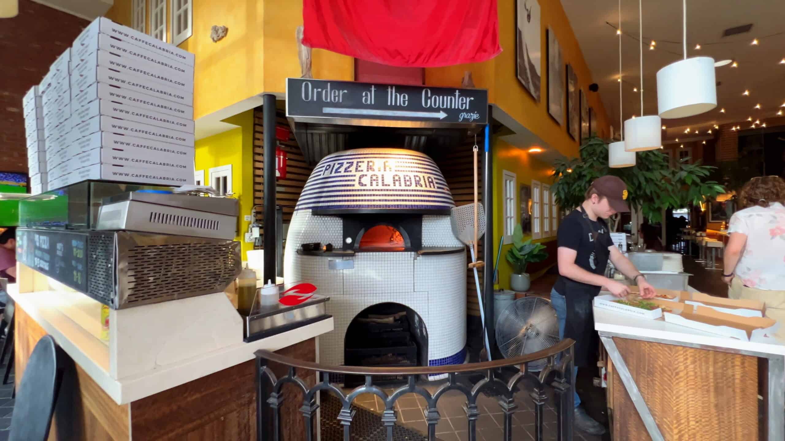 Freshly baked pizza being prepared at Point North Park restaurant in San Diego, California, with a traditional stone oven and vibrant interior decor.