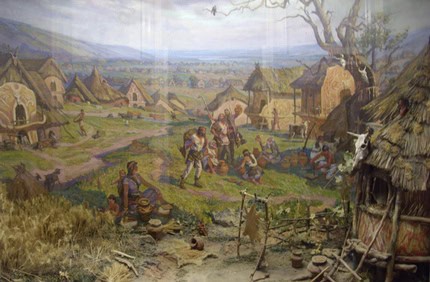 Древнє поселення з хатами та людьми у природному середовищі.