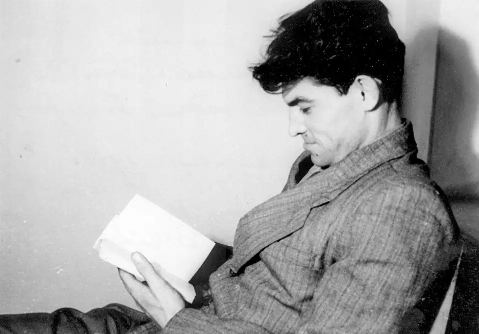 Василь Стус читає книгу, сидячи на стільці у чорнобілому фото.