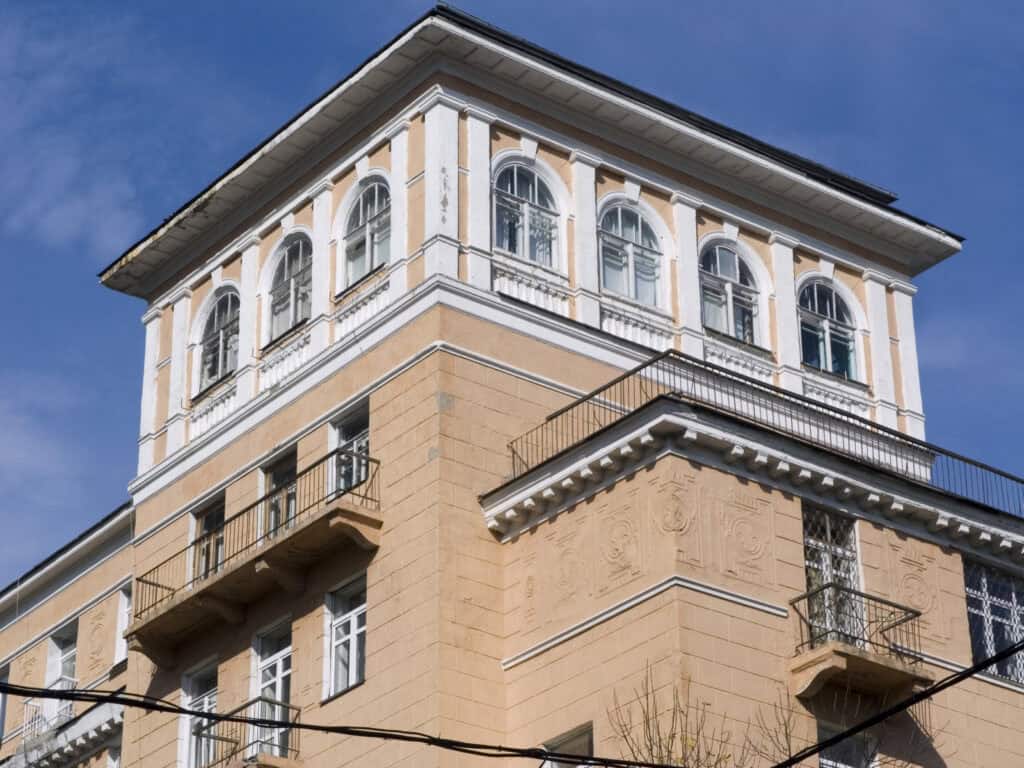 Історична будівля з архітектурними деталями та балконами, зображена на яскравому фоні неба.
