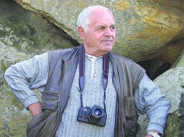 Портрет Юрія Іллєнка на природі з камерою на шиї.