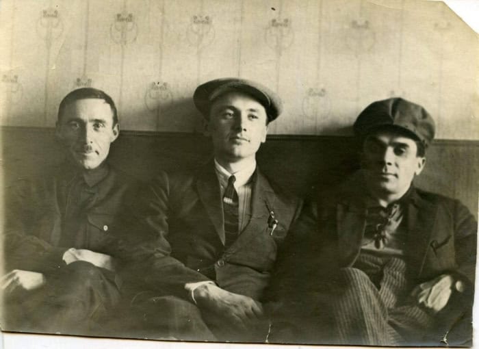Три чоловіки в старовинних капелюхах і костюмах, сидять разом у фотостилі.