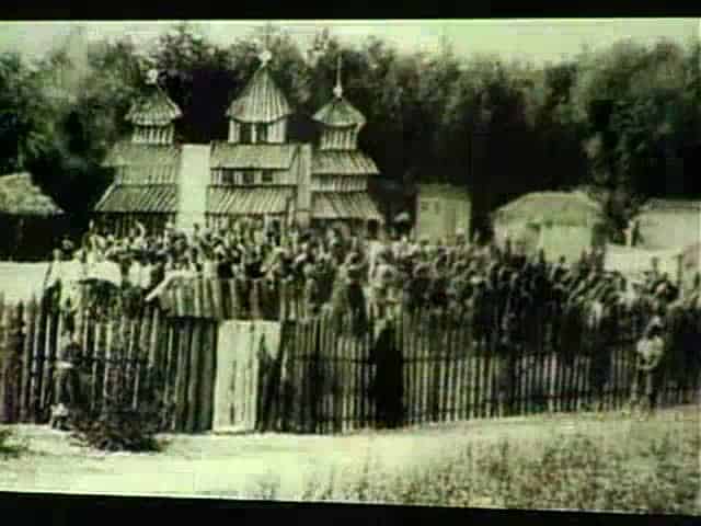 Історична фотографія українського села з дерев'яною церквою та людьми на подвір'ї.