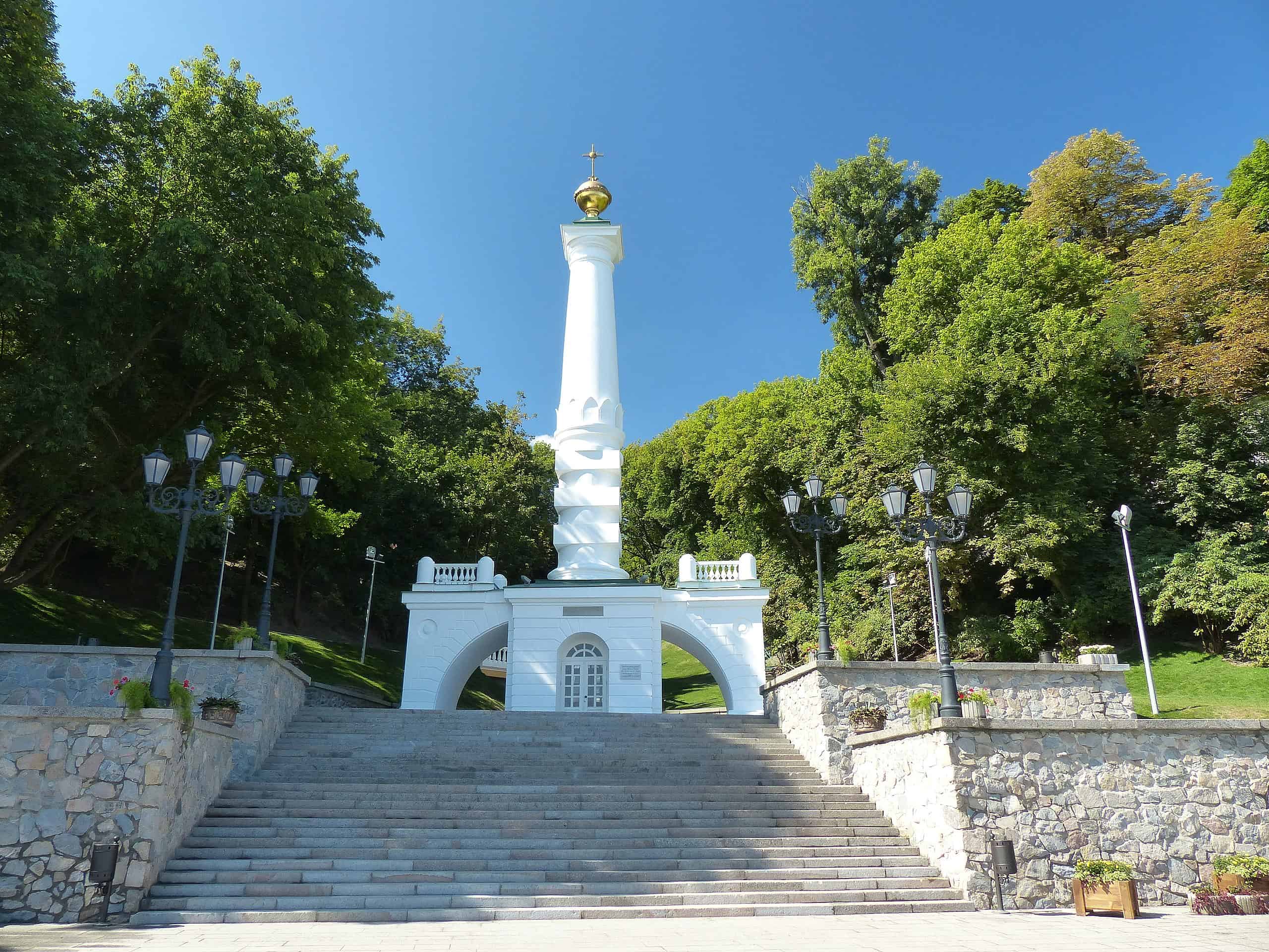 Пам'ятник у Києві на фоні зелених дерев і ясного неба.