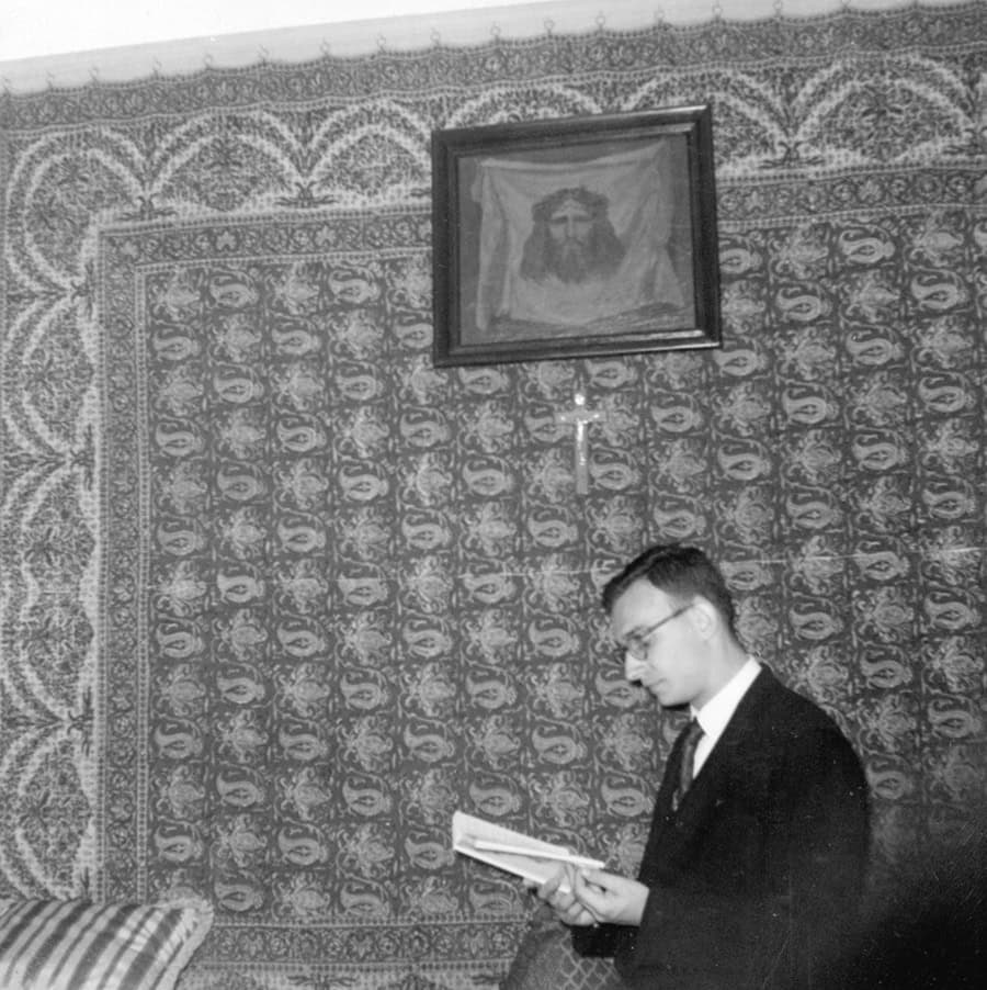 Молодий чоловік читає книгу в кімнаті з іконою і портретом Ісуса Христа на стіні.