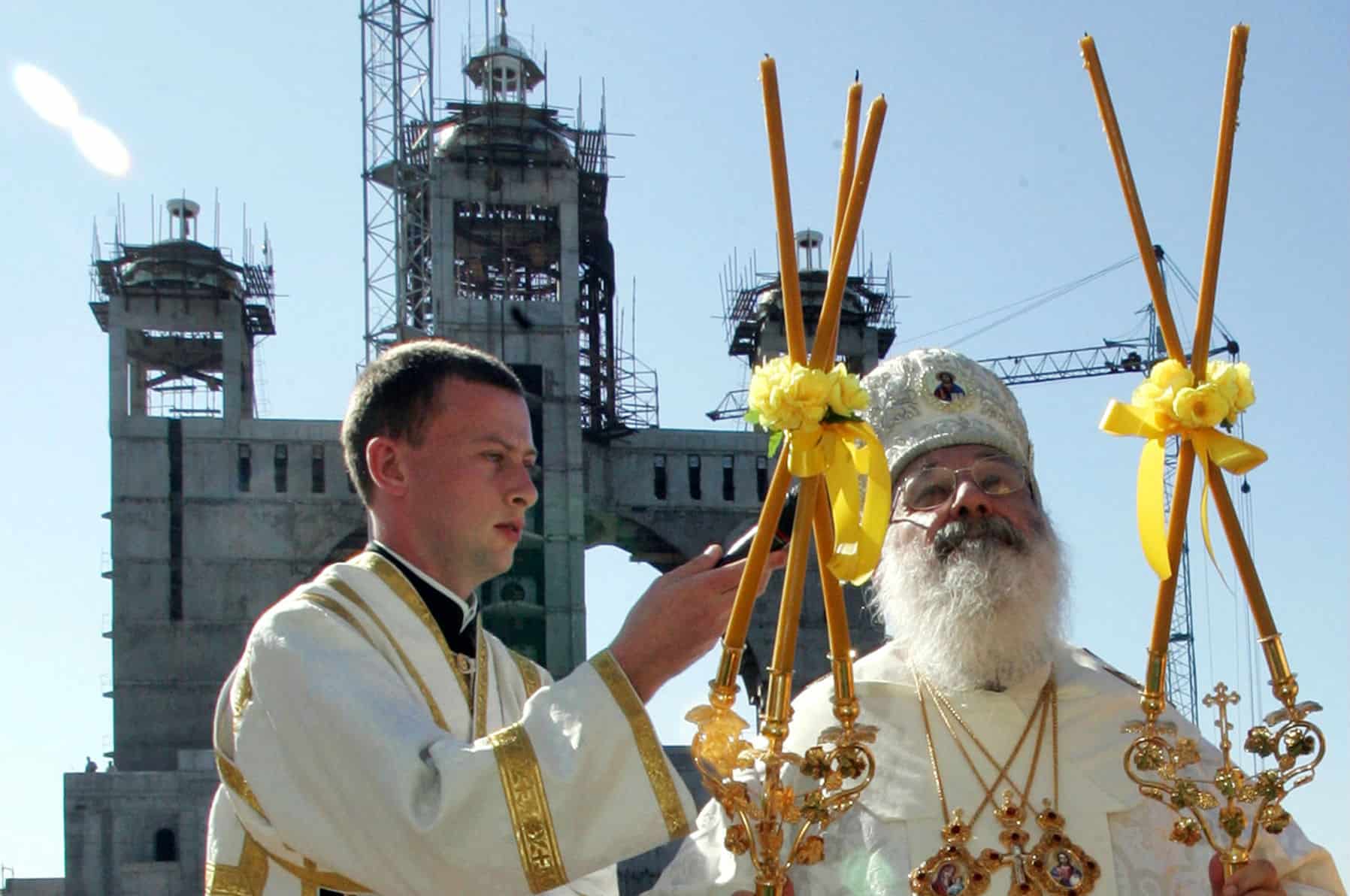 Українські церковні служителі з церковними свічками на фоні церкви.