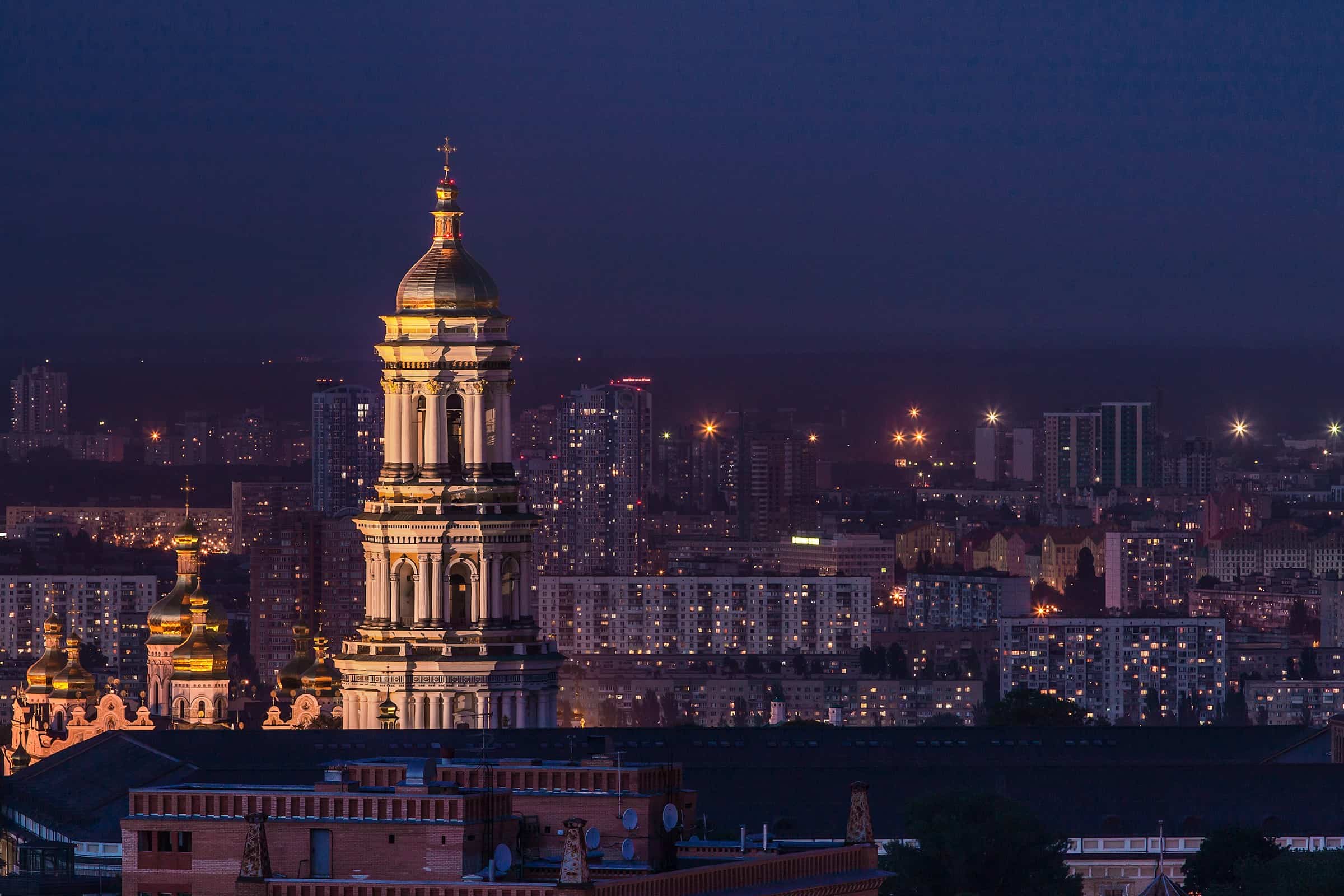 Київська церква з золотим куполом на тлі міста вночі.