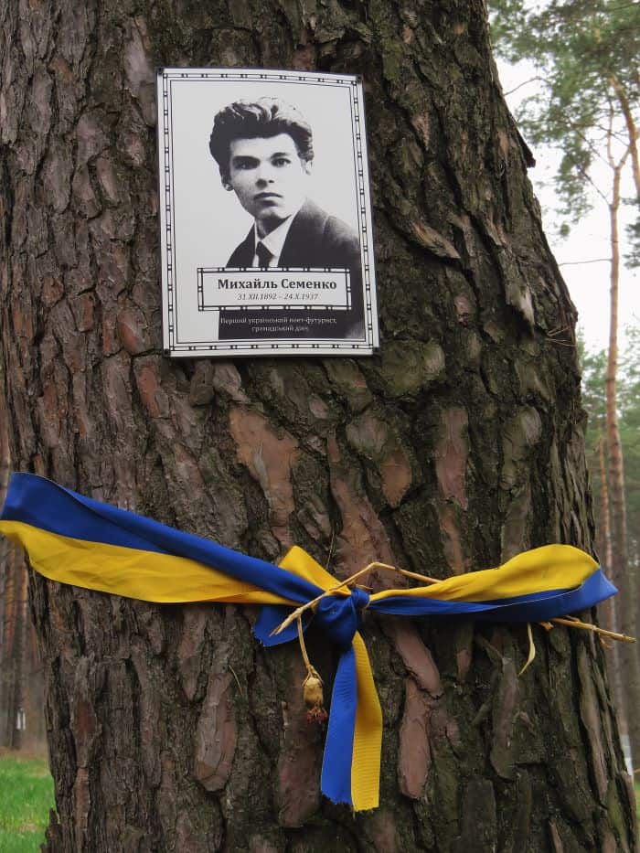 Пам'ятна дошка Михайлю Семенку на дереві з жовто-синьою стрічкою.