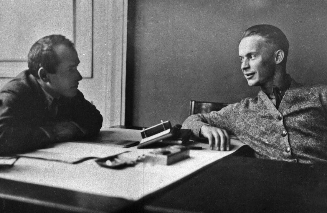 Двоє чоловіків спілкуються за столом у класичному стилі, історична фотографія.